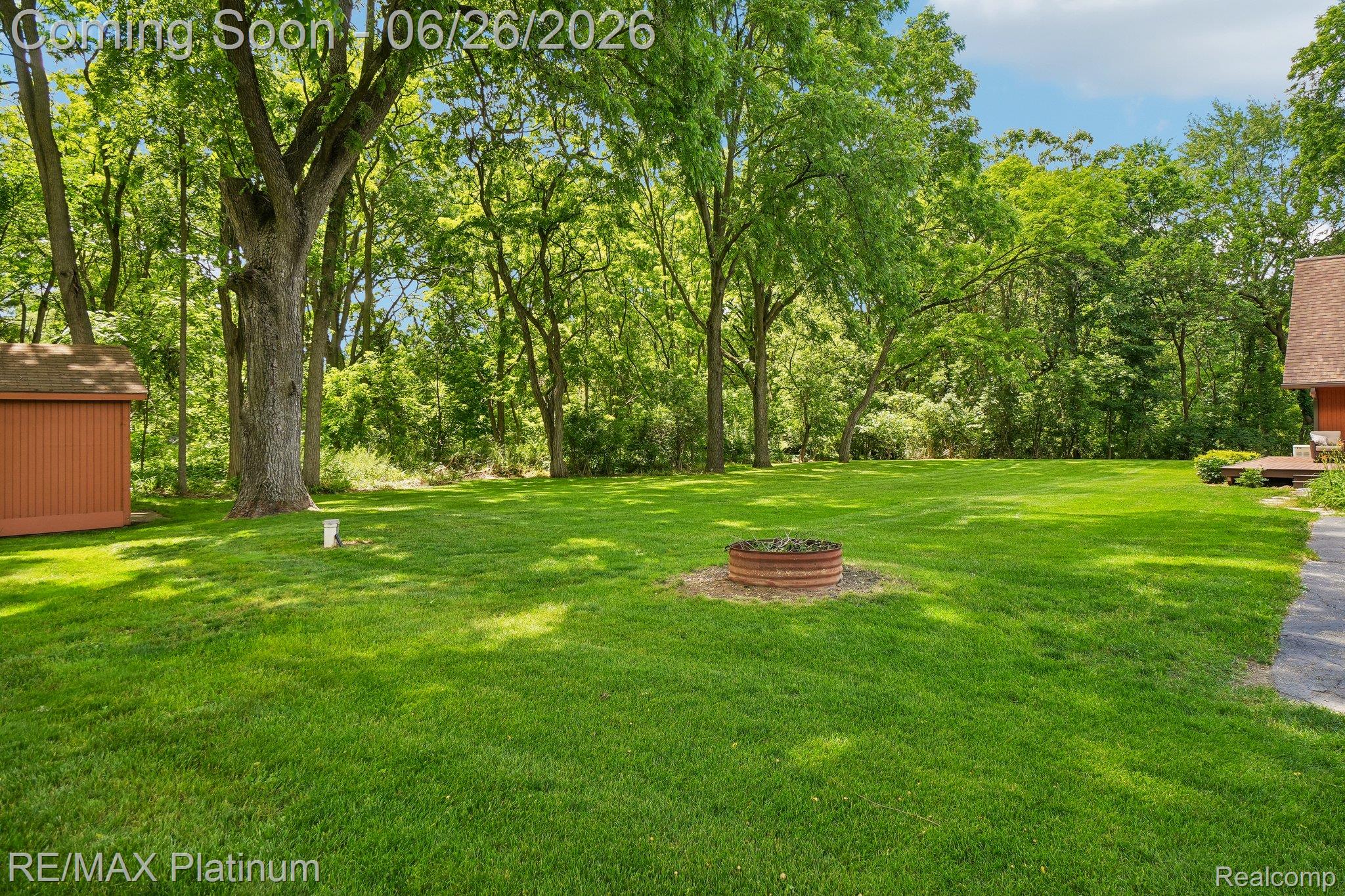 6100 Oak Valley Road Brighton, MI 48116 - Photo 36 of 47 Spacious backyard featuring a lush lawn, mature trees, a metal fire pit, and a detached storage shed