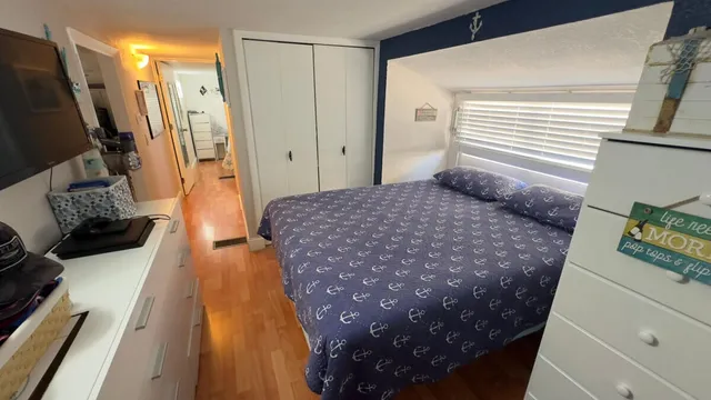 a bedroom with a bed wooden floor and a flat tv screen on dresser