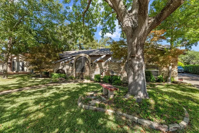 a backyard of a house with table and chairs under a large tree