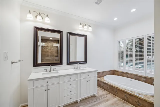 a bathroom with a tub a double vanity sink a window a mirror and