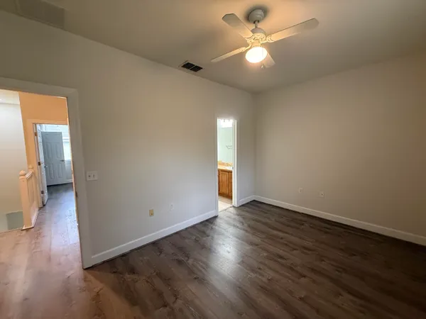 a view of an empty room with wooden floor and a ceiling fan