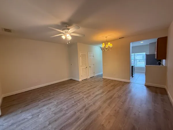 a view of an empty room with wooden floor and a ceiling fan