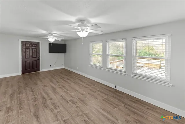an empty room with wooden floor fan and windows