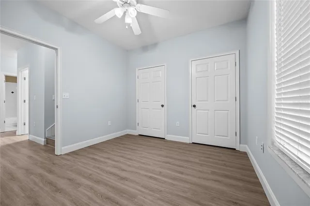 an empty room with wooden floor chandelier fan and windows