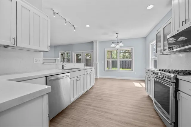 a kitchen with stainless steel appliances granite countertop a stove top oven a sink a refrigerator white cabinets and wooden floor