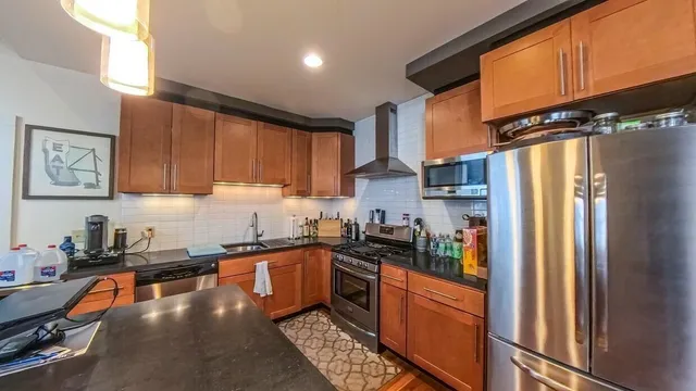 a kitchen with stainless steel appliances granite countertop a refrigerator a sink dishwasher a stove top oven a refrigerator and cabinets