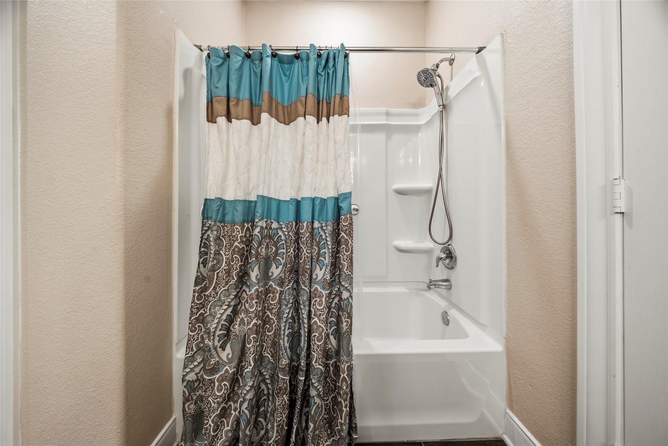 105 West Point Way Elgin, TX 78621 - Photo 9 of 27 White fiberglass tub and shower combination with an integrated multi-shelf unit and a chrome shower head with handheld attachment