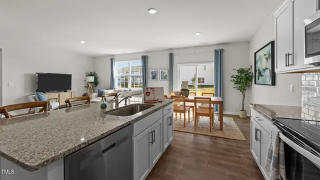 a living room with stainless steel appliances furniture wooden floor and a kitchen view