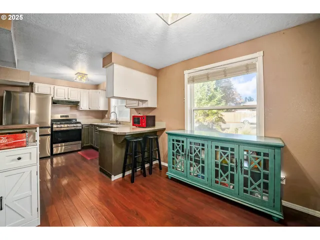 a open kitchen with stainless steel appliances granite countertop a stove top oven a refrigerator a dining table and chairs with wooden floor