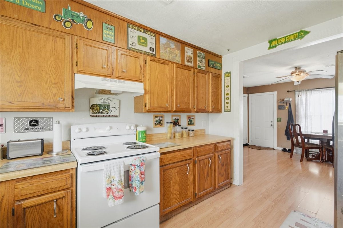 765 Norcross Road Wallis, TX 77485 - Photo 10 of 42 This kitchen features warm wood cabinetry, a white electric stove, and decorative vintage-style signs. It opens into a cozy dining area with light wood floors and ample natural light.