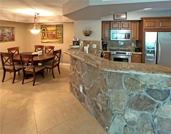 a dining hall with stainless steel appliances kitchen island granite countertop a table and chairs in it