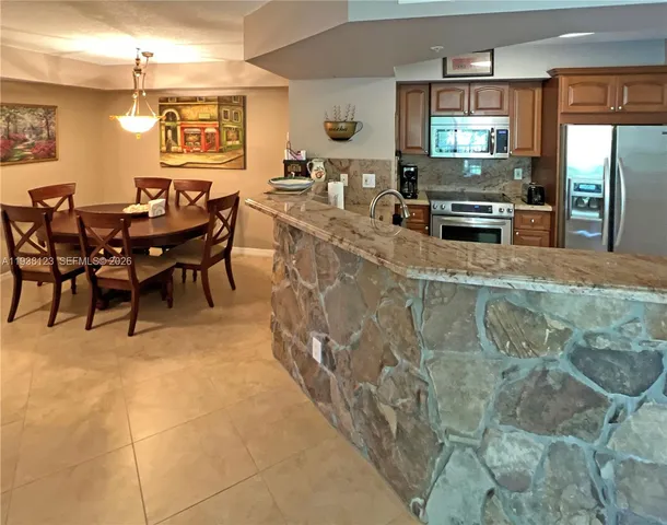 a dining hall with stainless steel appliances kitchen island granite countertop a table and chairs in it