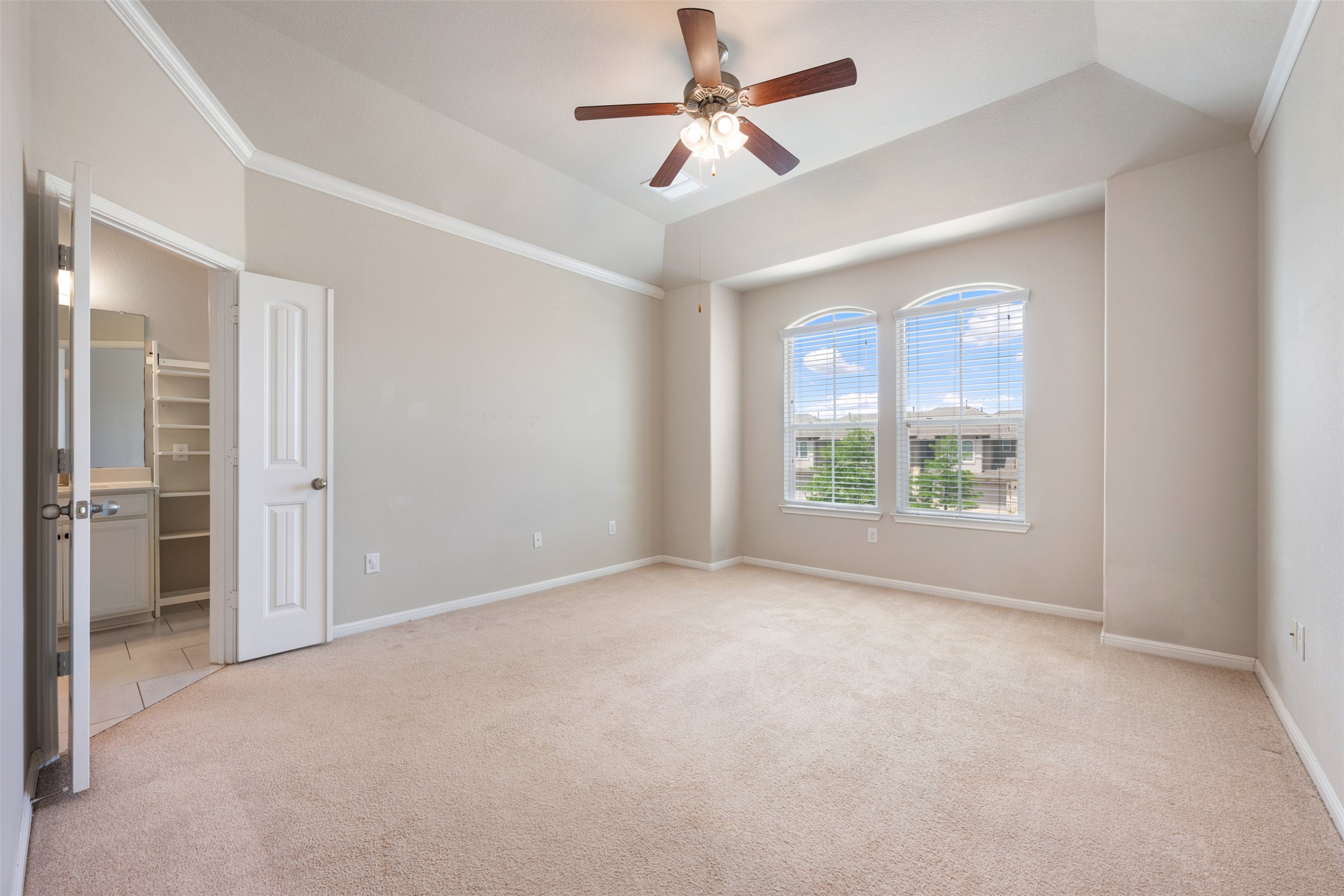 211 Parable Cove Pflugerville, TX 78660 - Photo 22 of 40 Spacious bedroom featuring neutral carpeting, a tray ceiling with crown molding, and two arched windows