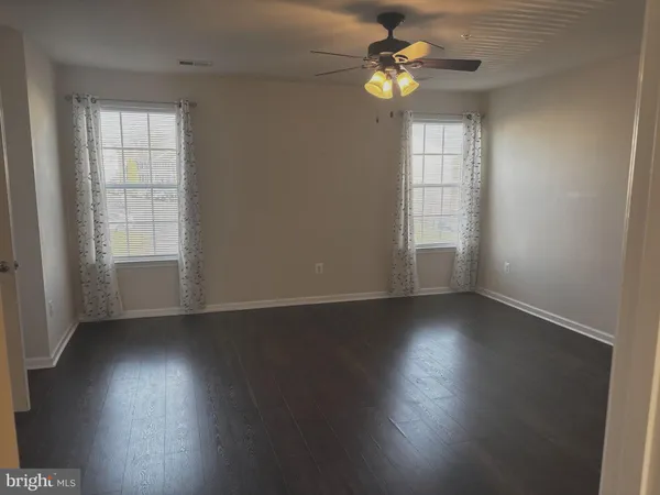 an empty room with wooden floor chandelier fan and windows