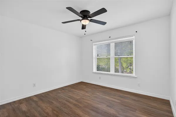 a view of an empty room with wooden floor and a ceiling fan
