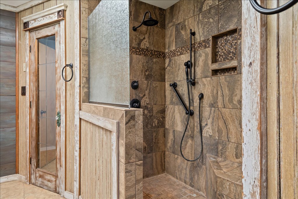 2421 Post Oak Road Webberville, TX 78653 - Photo 18 of 36 The walk in shower is fully tiled with a rich, natural stone look, features a built-in corner bench, and has both a fixed showerhead and a handheld wand.