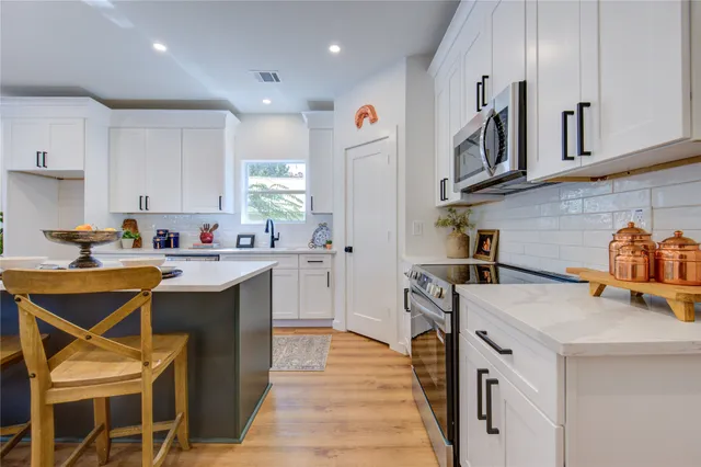 a open kitchen with stainless steel appliances kitchen island granite countertop a sink dishwasher a stove and white cabinets with wooden floor
