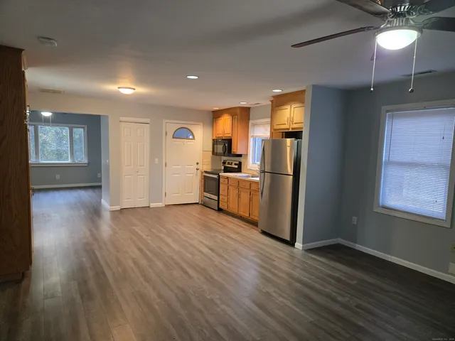 an empty room with wooden floor kitchen view and windows