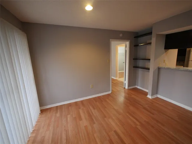 a view of empty room with wooden floor and kitchen