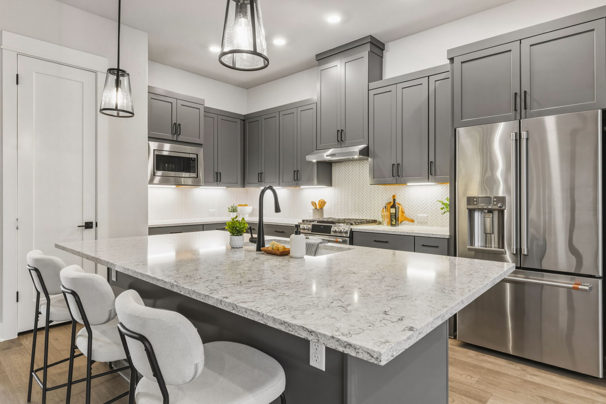 Kitchen featuring a spacious island with a light-toned countertop, gray cabinetry, stainless steel appliances, and a mosaic tile backsplash
