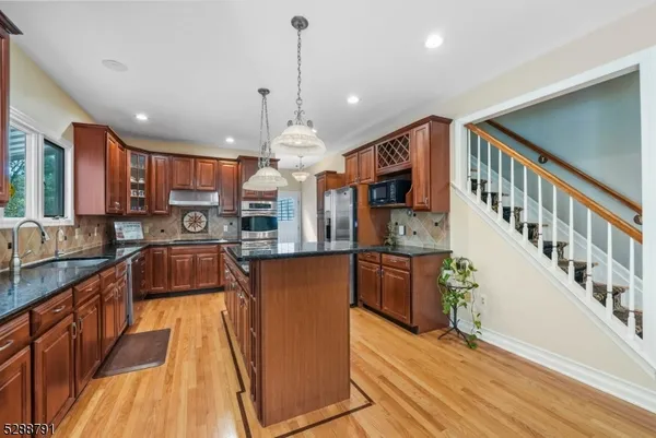 a kitchen with stainless steel appliances granite countertop a refrigerator a sink dishwasher a oven a large island with wooden floor and cabinets