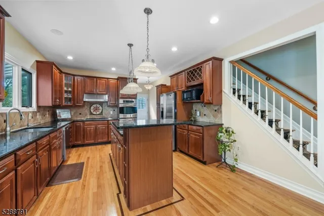 a kitchen with stainless steel appliances granite countertop a refrigerator a sink dishwasher a oven a large island with wooden floor and cabinets