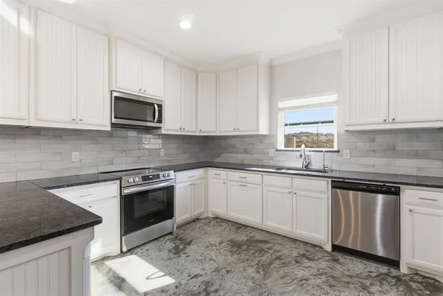 a kitchen with granite countertop white cabinets sink and stainless steel appliances