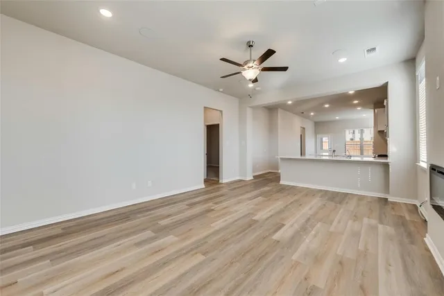 a view of an empty room with wooden floor and a kitchen