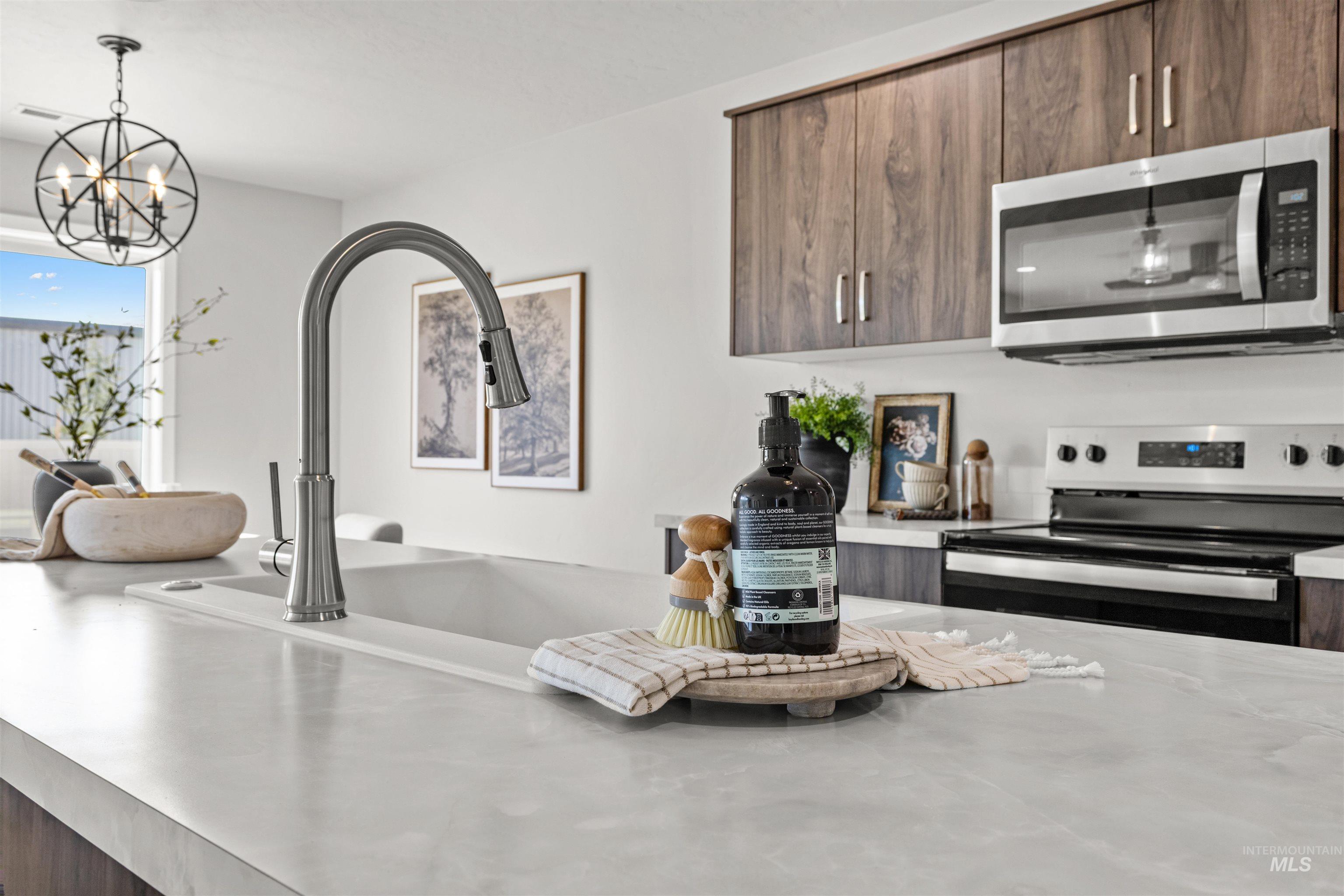 2534 West Fallon Loop Nampa, ID 83651 - Photo 13 of 28 Kitchen view of modern cabinets, stainless steel appliances, dark wood finish cabinets, suspended lighting, and light stone counters