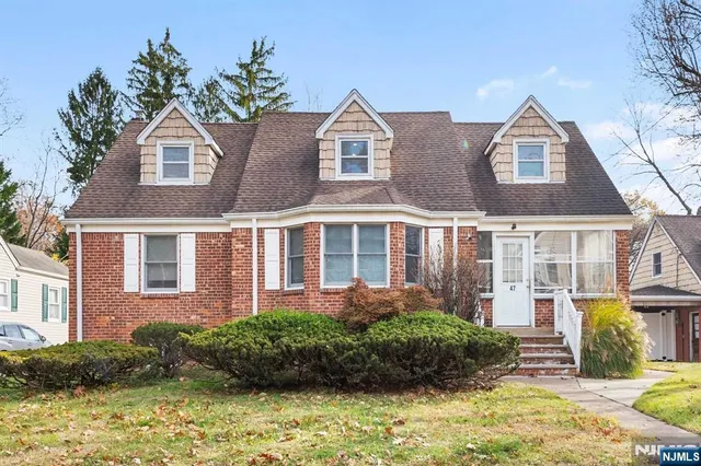 a view of a brick house with a yard plants and large tree