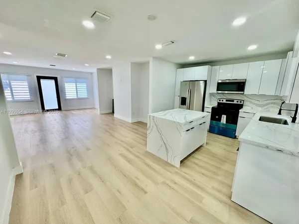 a large white kitchen with kitchen island a stove a refrigerator a oven and a sink with wooden floor