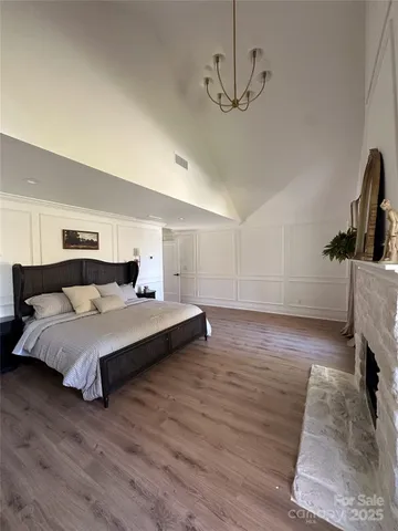 a spacious bedroom with a bed a chandelier and a dresser with wooden floor