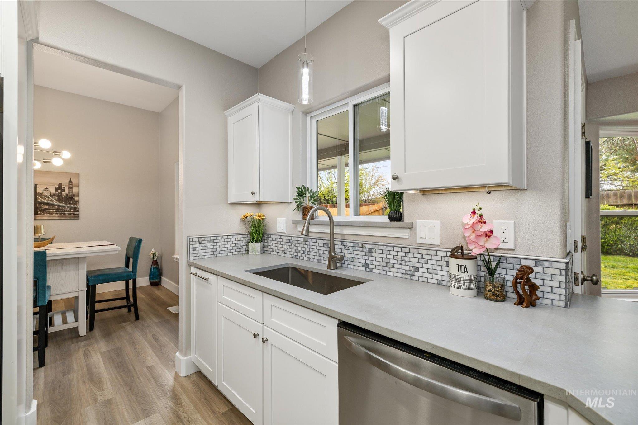 2250 North Amethyst Avenue Meridian, ID 83646 - Photo 16 of 50 Kitchen featuring white cabinetry, stainless steel dishwasher, light wood-style floors, tasteful backsplash, and decorative light fixtures