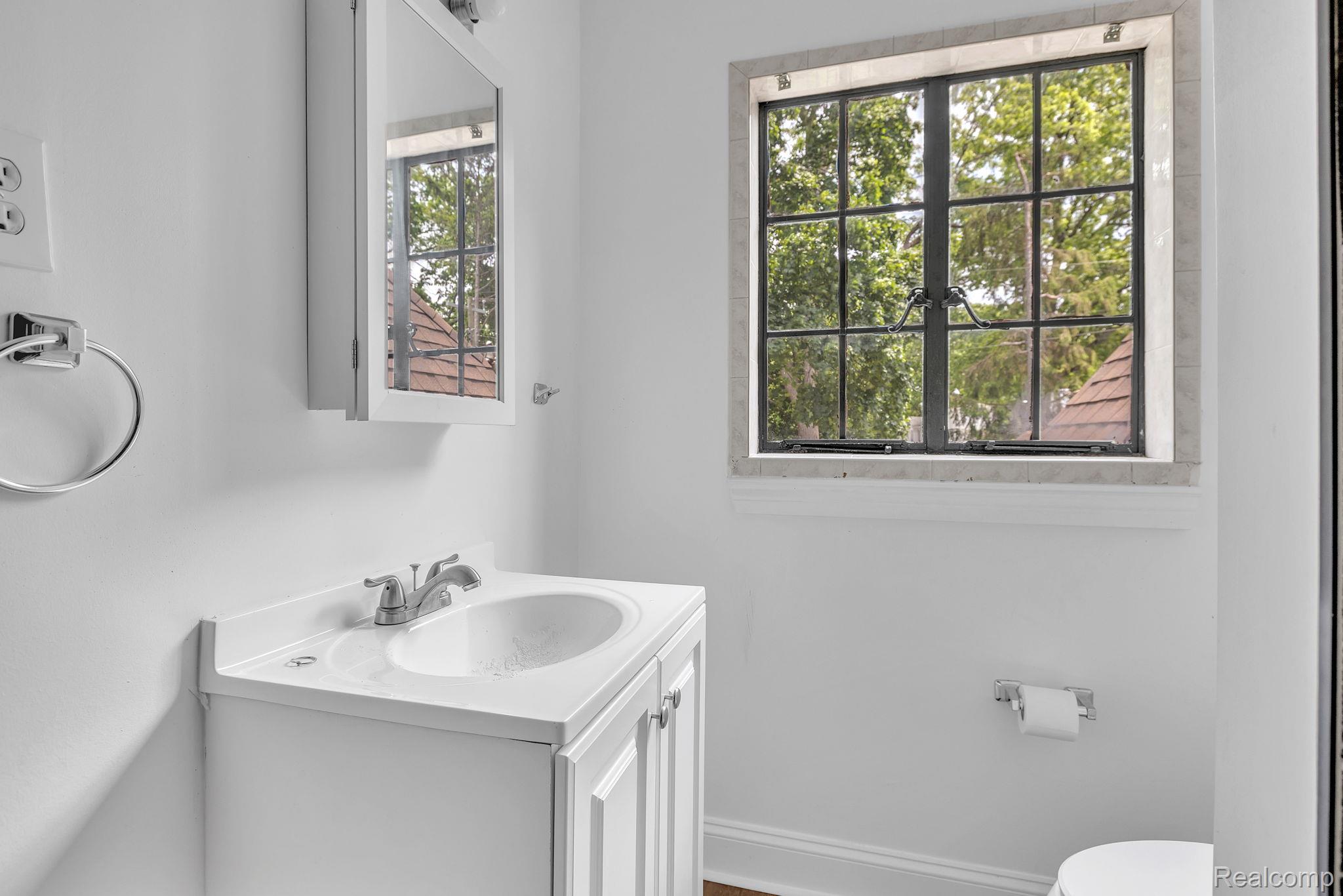 19510 Stratford Road Detroit, MI 48221 - Photo 35 of 45 Window with black grid mullions, surrounded by stone tile, featuring a white vanity with integrated sink, chrome faucet, and mirrored medicine cabinet