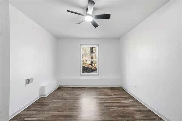 an empty room with wooden floor ceiling fan and windows