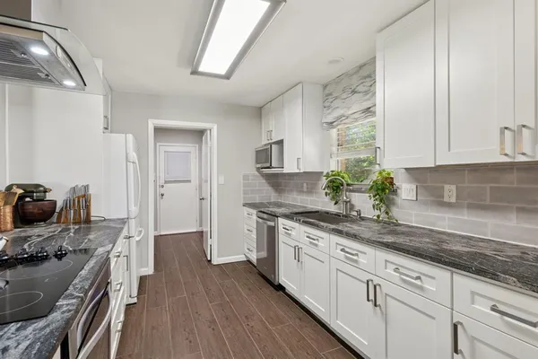a kitchen with stainless steel appliances granite countertop a stove a sink dishwasher and white cabinets with wooden floor