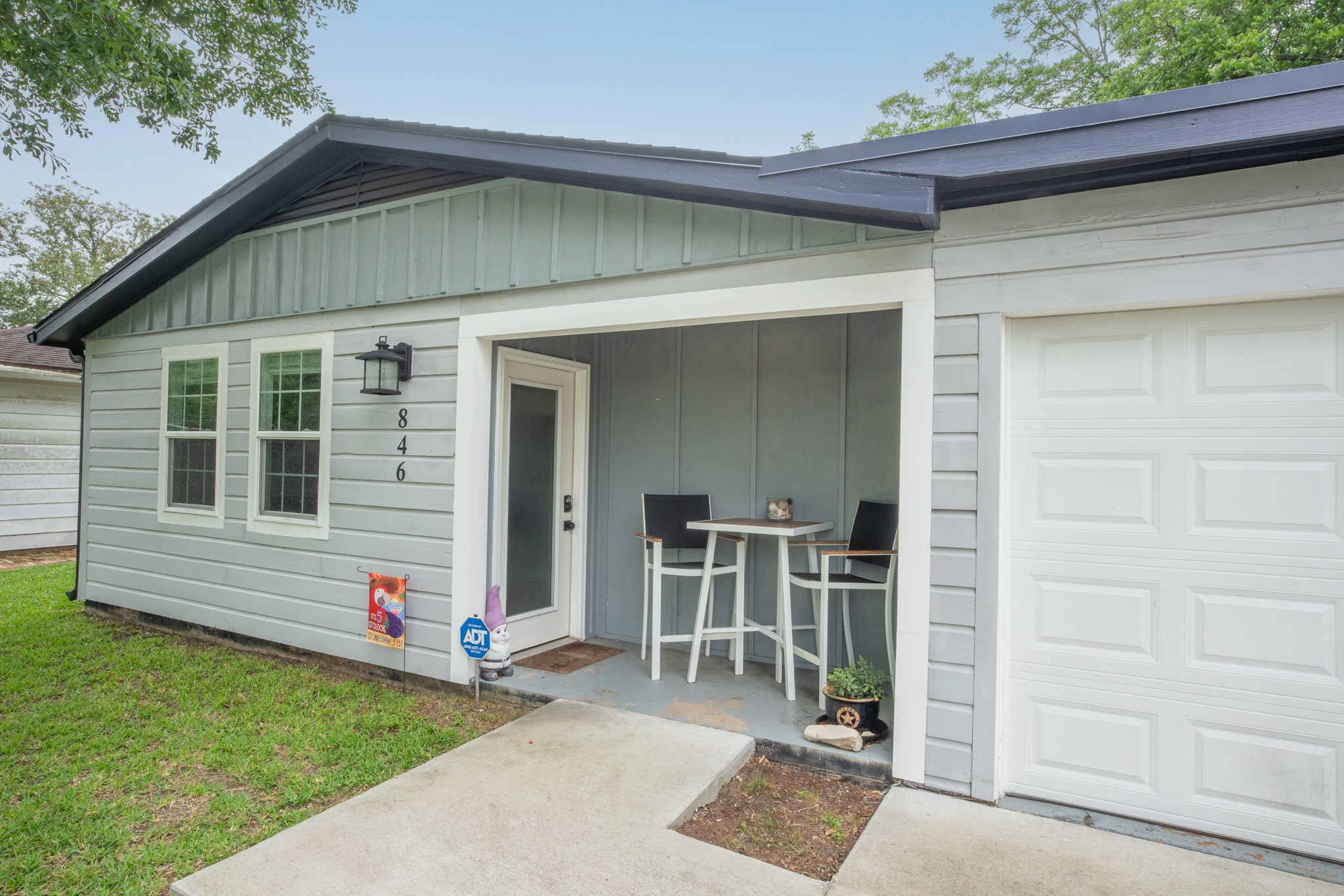 846 South Anderson Street Angleton, TX 77515 - Photo 2 of 30 Charming single-story home with a cozy front porch, featuring a small seating area. The exterior offers a modern, clean look with light gray siding and a welcoming entrance.