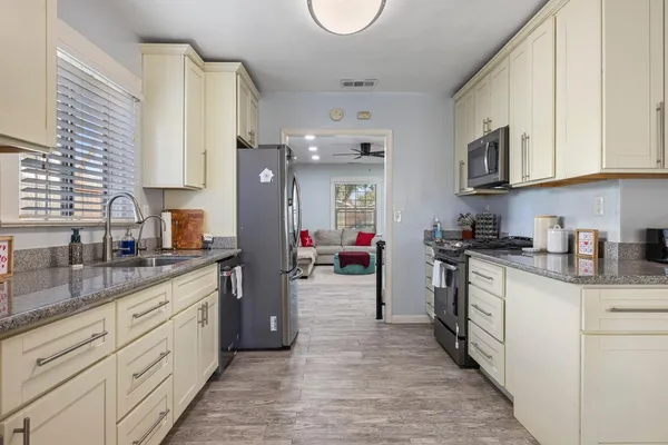 a kitchen with stainless steel appliances granite countertop a sink dishwasher stove and white cabinets with wooden floor