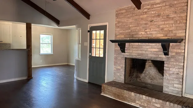 an empty room with wooden floor fireplace and windows