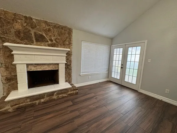 a view of an empty room with wooden floor fireplace and a window