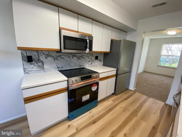 a kitchen with stainless steel appliances a stove a microwave a refrigerator a sink and white cabinets