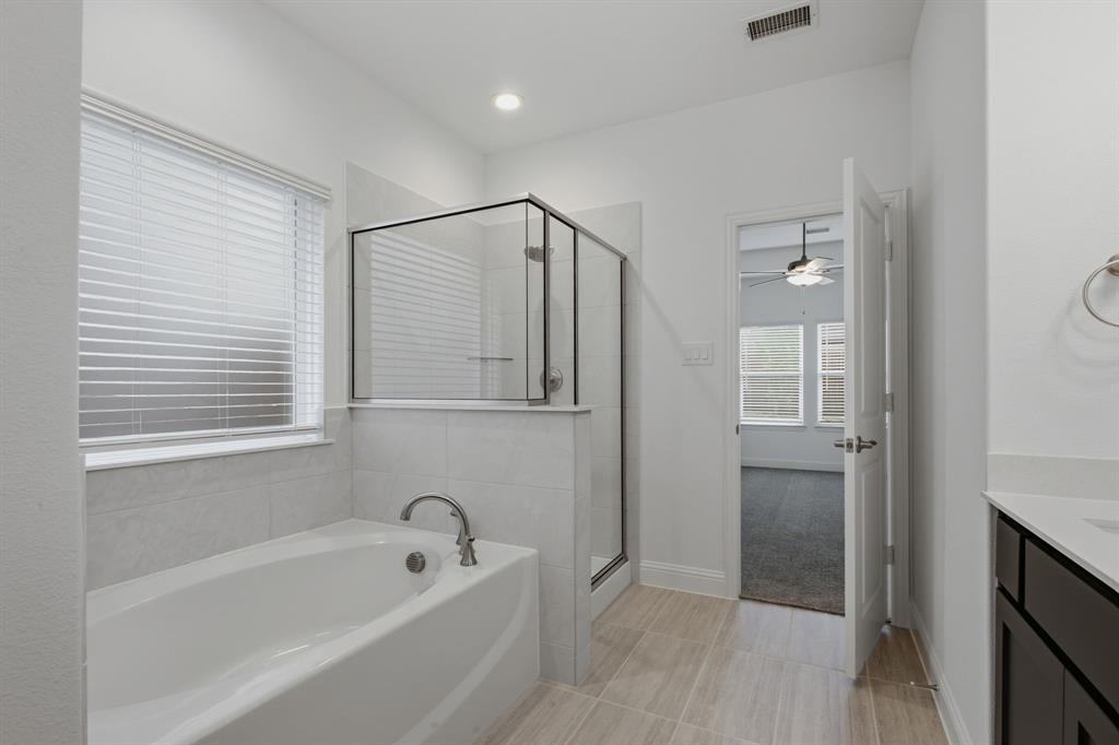 2911 Hanscom Street Forney, TX 75126 - Photo 31 of 40 Bright bathroom featuring a soaking tub, glass-enclosed shower, white tile surround, and wood-finish flooring