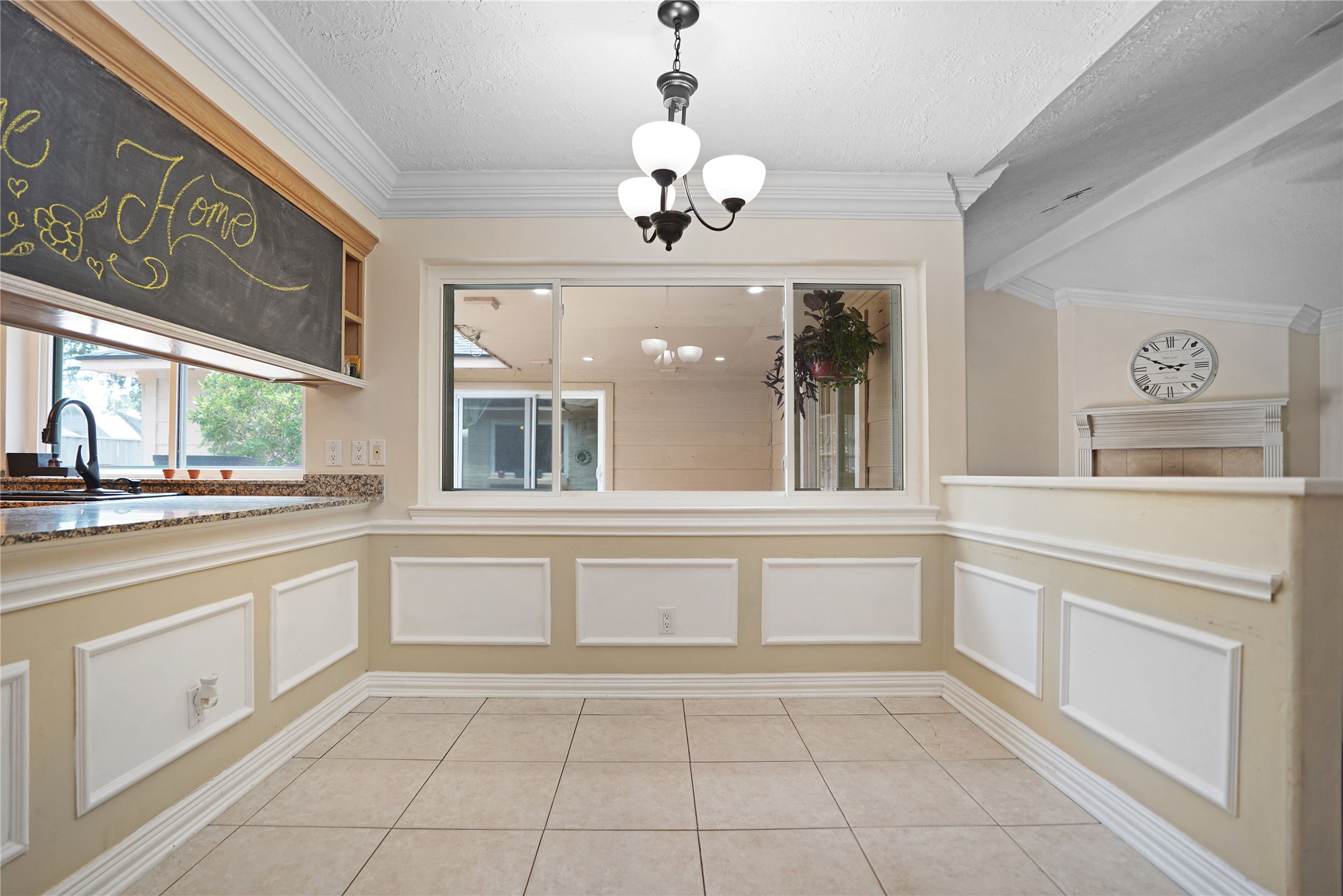 17119 Mellow Ridge Drive Spring, TX 77379 - Photo 8 of 32 A bright dining area featuring a large window, elegant wainscoting, and tile flooring. It includes a chalkboard accent, a classic chandelier, and an adjoining kitchen with a granite countertop.