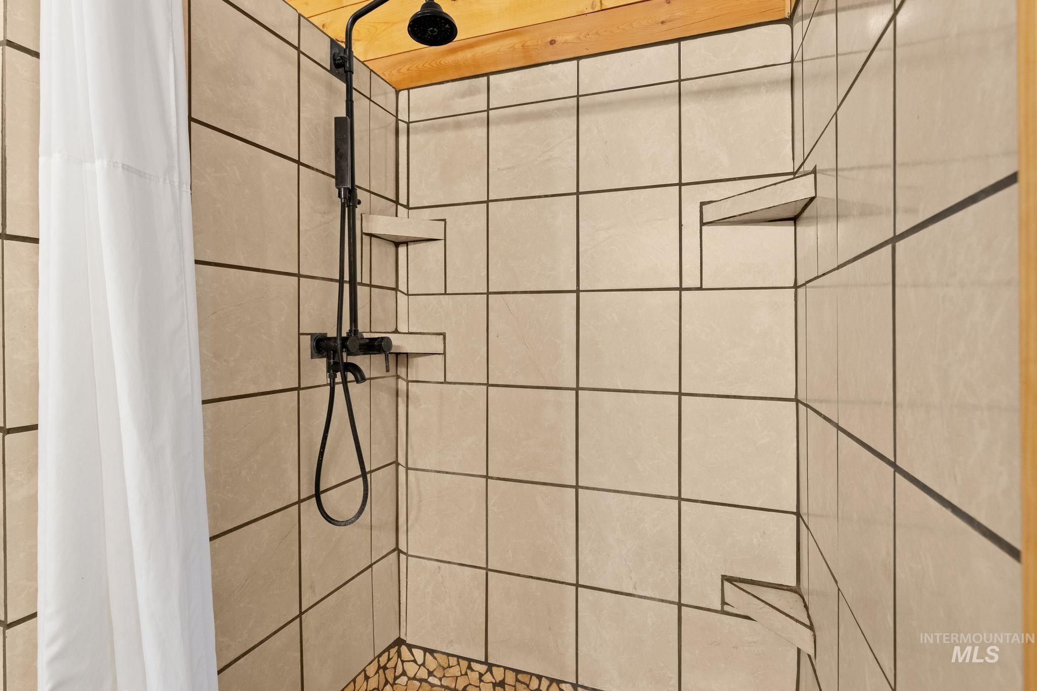 3989 East Mountain Road Anatone, WA 99401 - Photo 21 of 49 Tiled shower with a rainfall showerhead, handheld sprayer, and built-in shelving