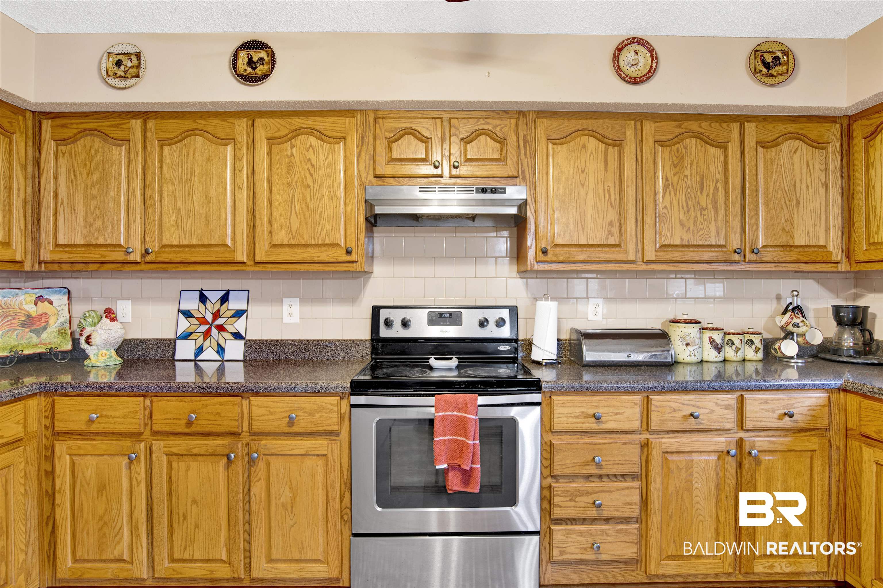 36434 Alexandria Trail Stapleton, AL 36578 - Photo 23 of 27 Kitchen with electric range, backsplash, under cabinet range hood, brown cabinetry, and dark stone counters