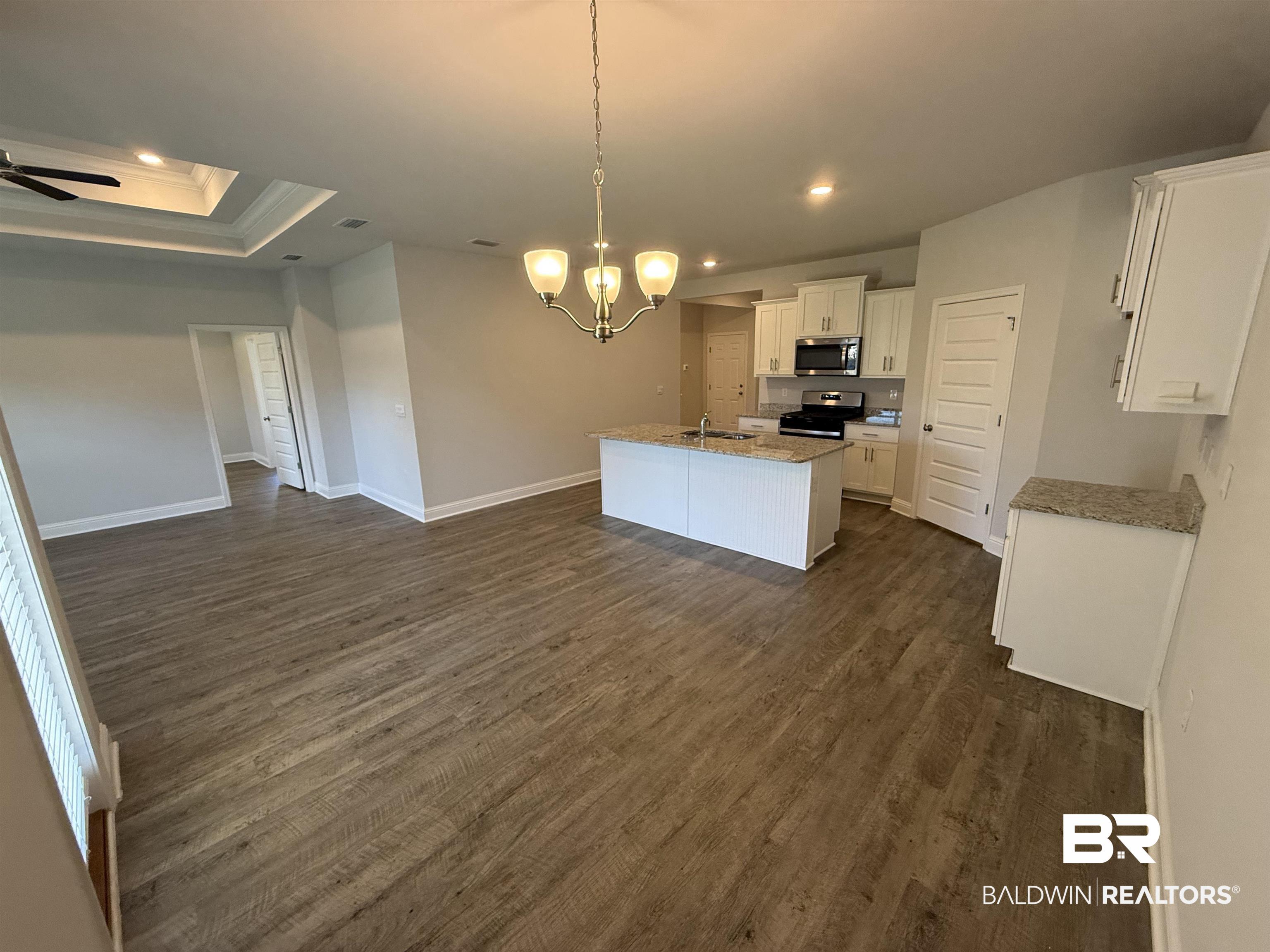23247 Lieutenant Avenue Foley, AL 36535 - Photo 22 of 47 Open-concept living space featuring wood-finish flooring, a tray ceiling with a fan, and a kitchen island with stone countertops