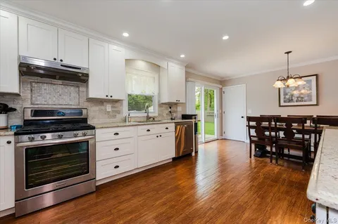 a kitchen with stainless steel appliances a stove a sink dishwasher and a dining table with wooden floor