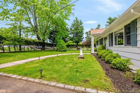 a view of a white house with a big yard and potted plants and large trees