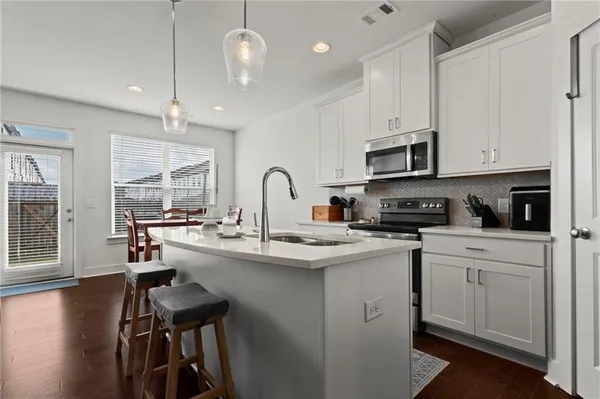 a kitchen with stainless steel appliances granite countertop a sink a stove a refrigerator cabinets and a dining table with wooden floor