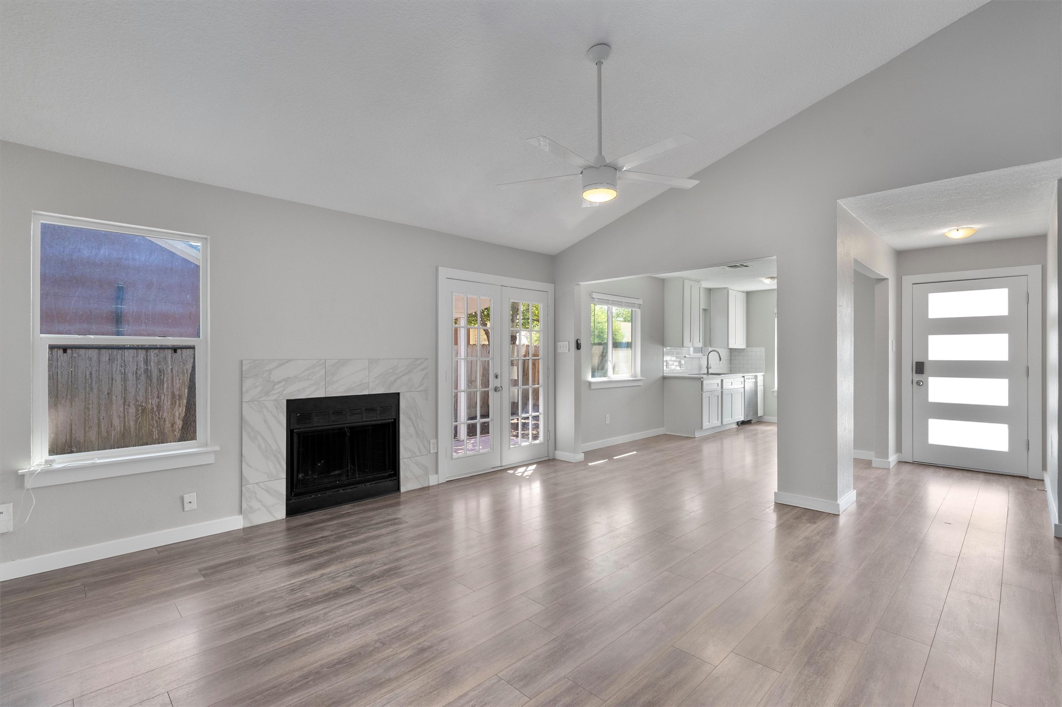 12321 Emery Oaks Road Austin, TX 78758 - Photo 3 of 27 A well-lit, spacious living space features vaulted ceilings, natural light, a cozy fireplace, French doors leading to outdoor relaxation, looking into the eat-in kitchen.
